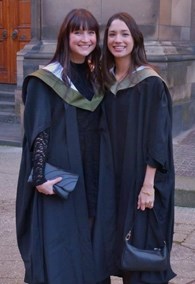 A photo of Emma and Dhanishtha standing both in their graduation gowns.