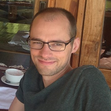 A close up photo of Nick in a cafe with a cup in the background.