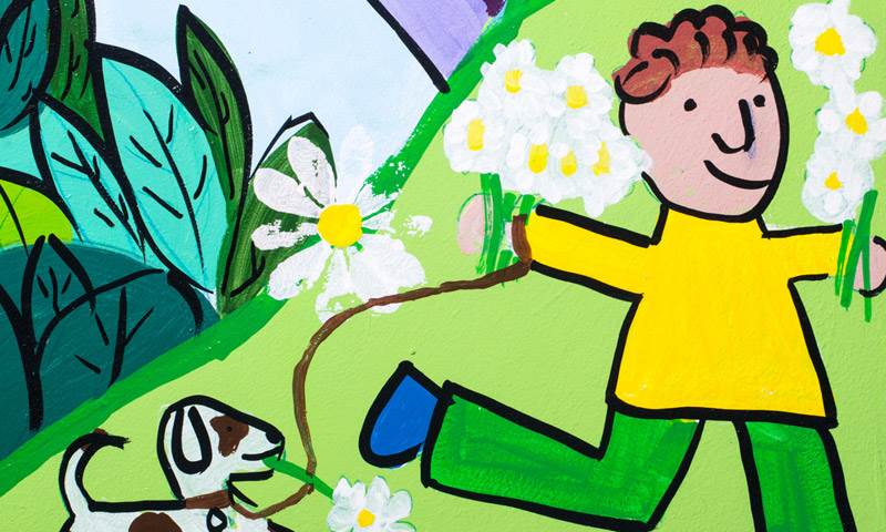 Mural shows child running through a flower meadow with their dog