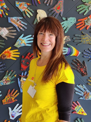 Director, Juliet Harris with a yellow top and lanyard. A collection of hands in the background.