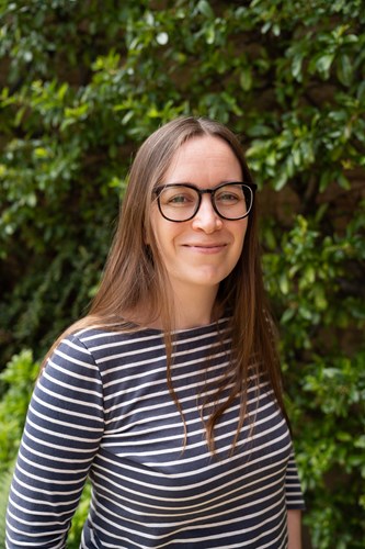 Photo of Mary, UNCRC Implementation Officer, wearing a stripped top. Greenery in the background.