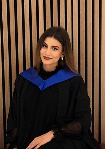 Photo of Marianiki sitting in graduation gown with a wooden style background.